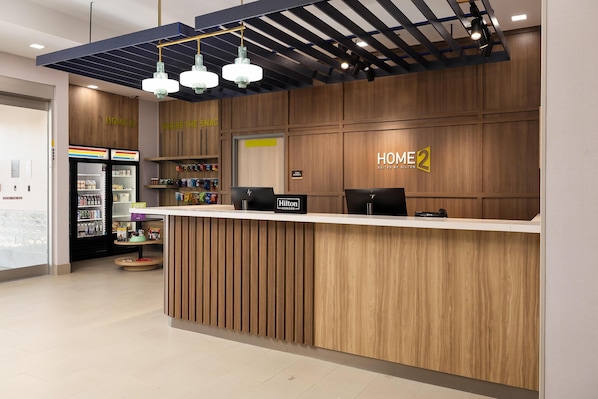Un mostrador de recepción de hotel con detalles de madera, un minibar y un letrero que indica 'HOME 2' suites.