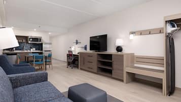 A modern living room with a sofa, a TV, a desk, and a kitchen area in the background.