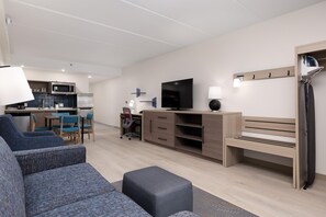 A modern living room with a sofa, a TV, a desk, and a kitchen area in the background.
