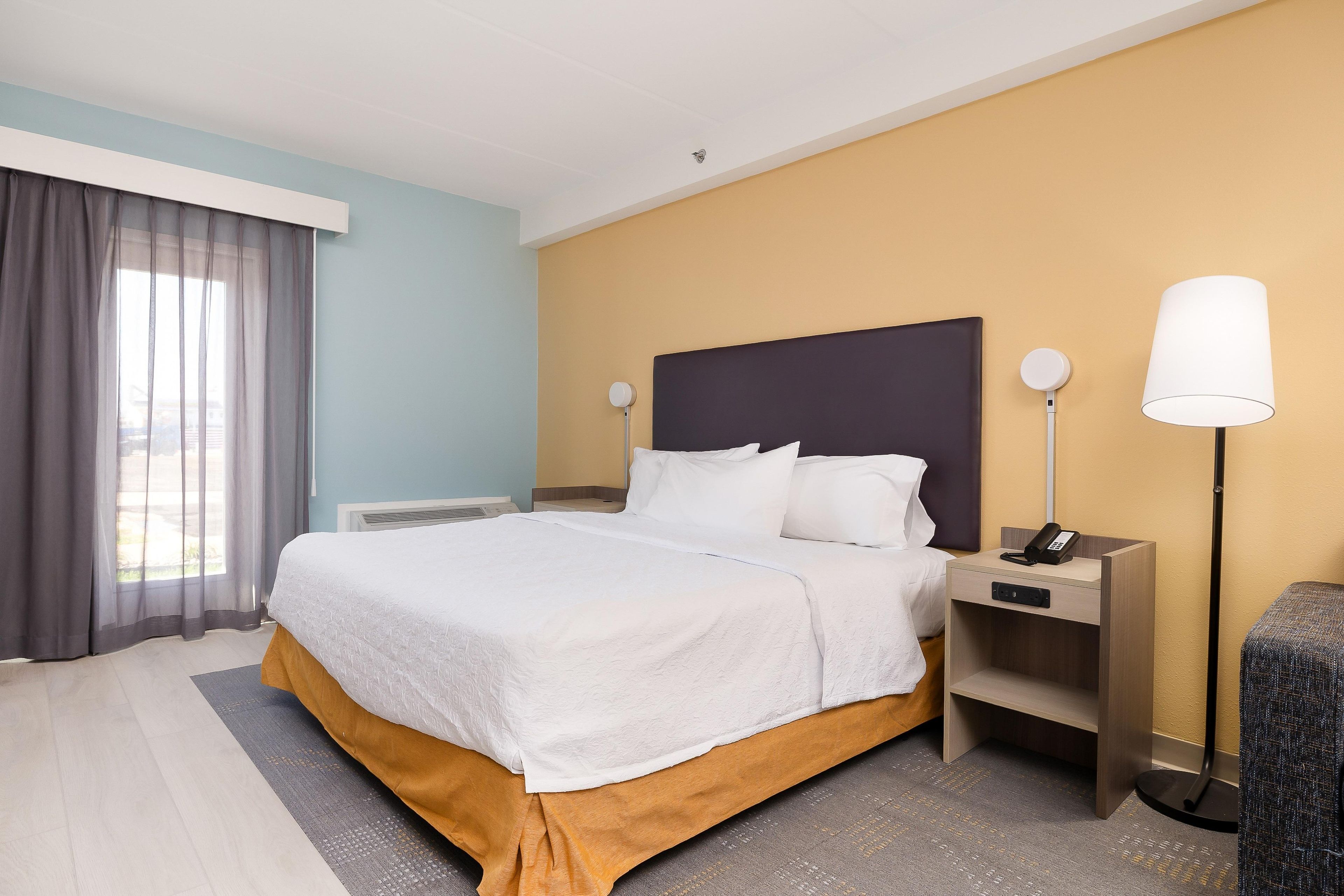 Una habitación de hotel con una cama grande, mesitas de noche, un escritorio y una lámpara.