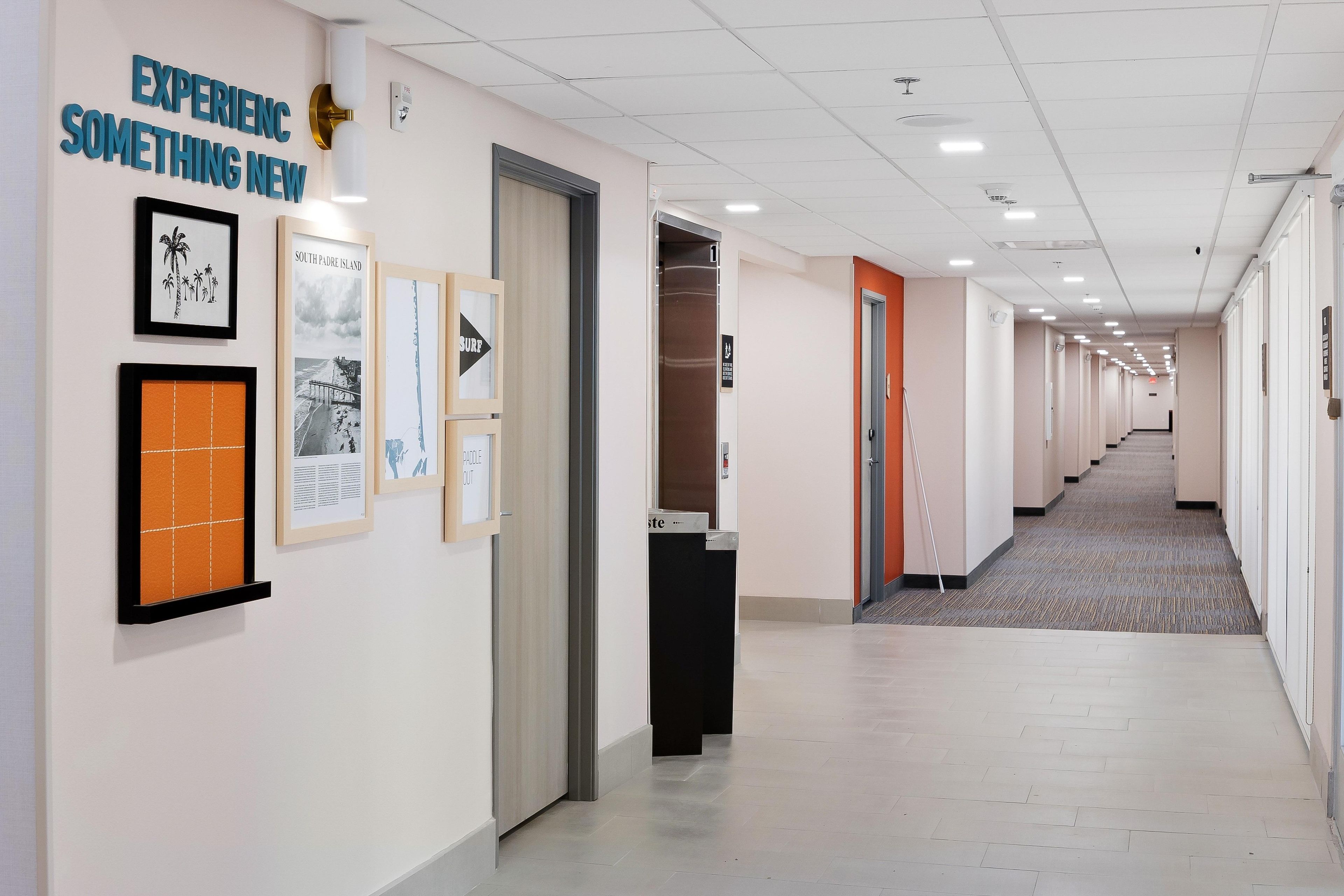 A hallway with framed pictures on the walls, a sign that says 'EXPERIENC SOMETHING NEW', and a door with a sign that says 'PADDLE OUT'.