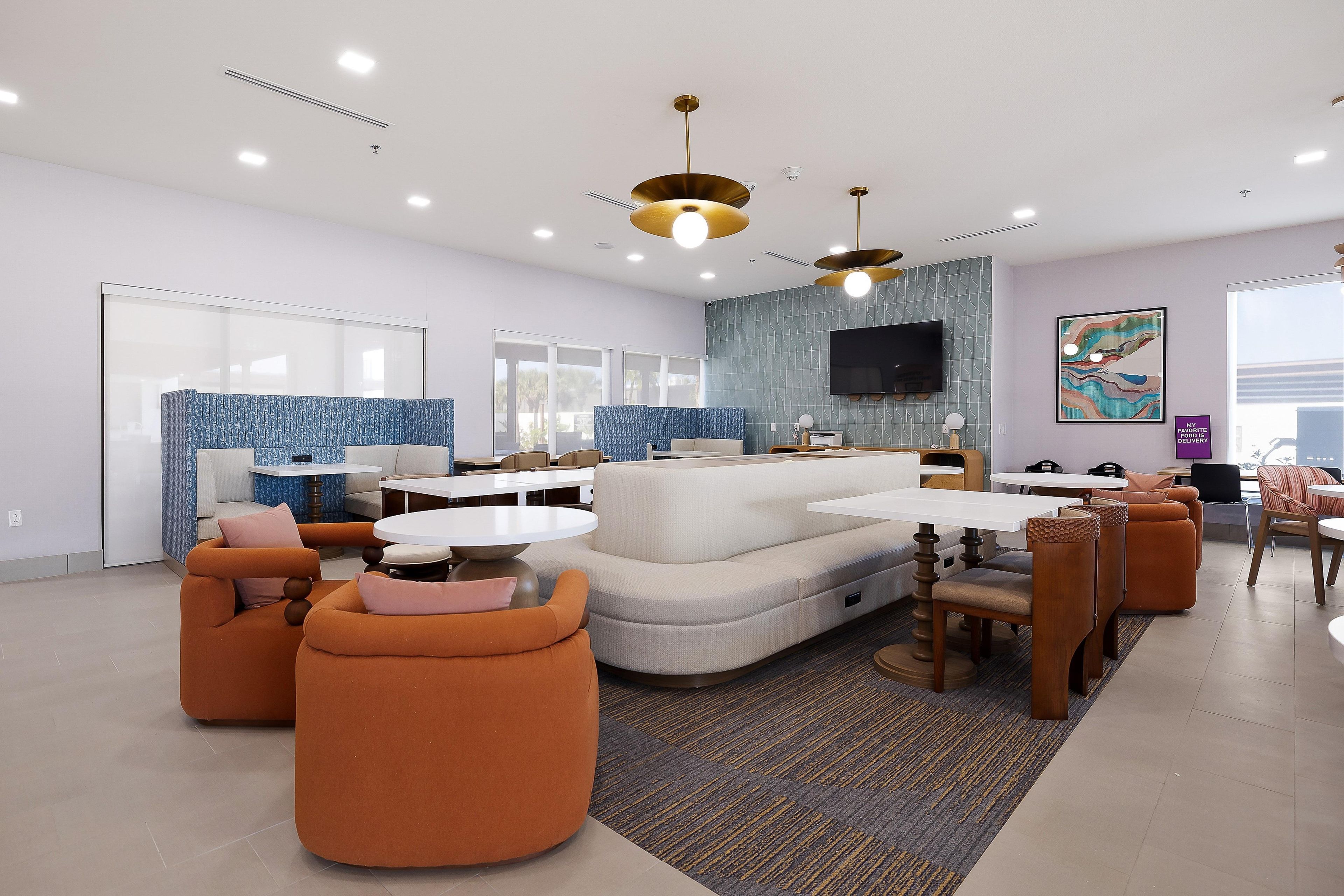 Un salon moderne avec un canapé d’angle, des fauteuils orange, un téléviseur à écran plat et un mur orné d’un motif.