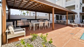 Un patio exterior con una parrilla, asientos y una piscina.