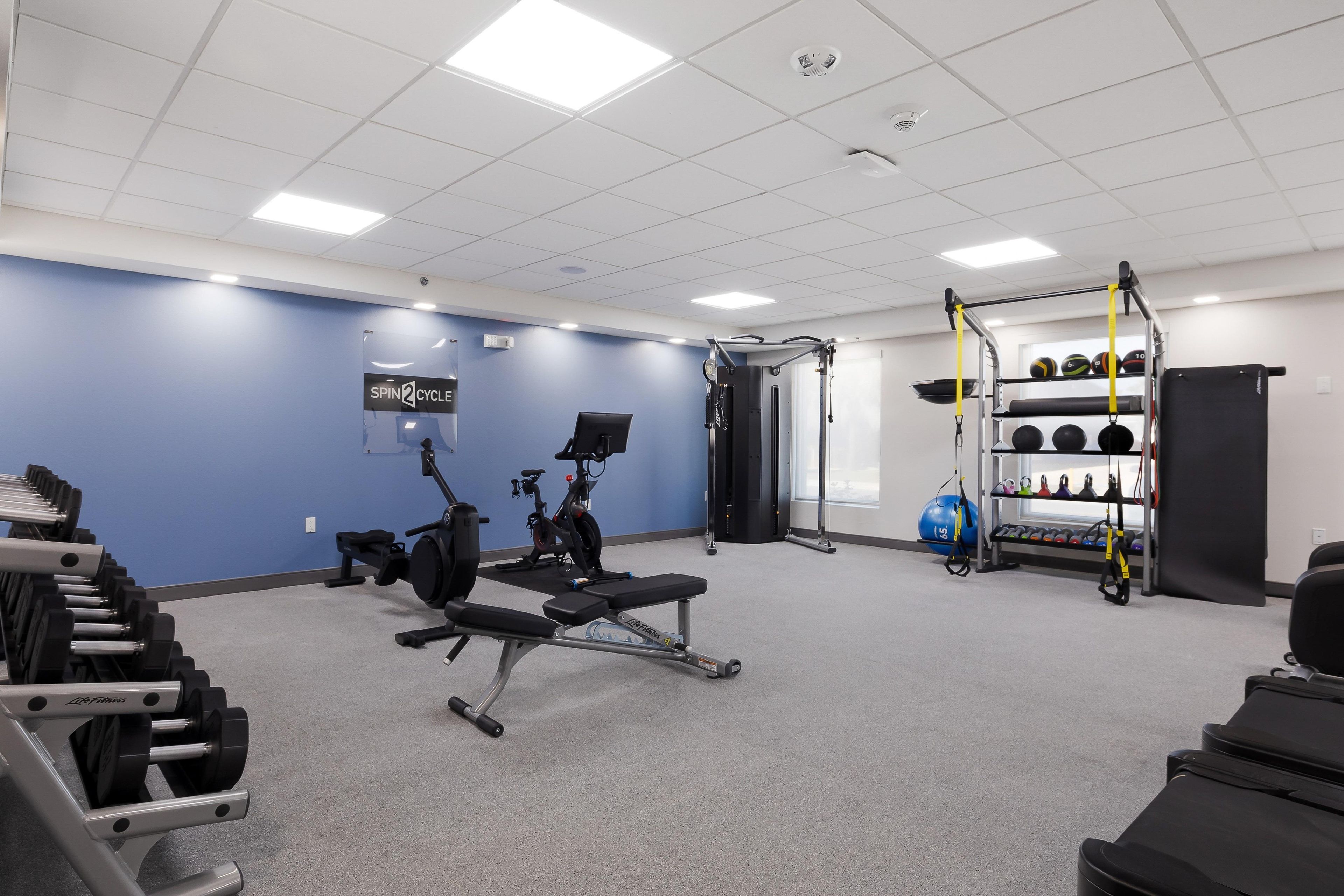 Une salle de sport équipée de machines d’exercice, avec un panneau fixé au mur et un porte-poids.