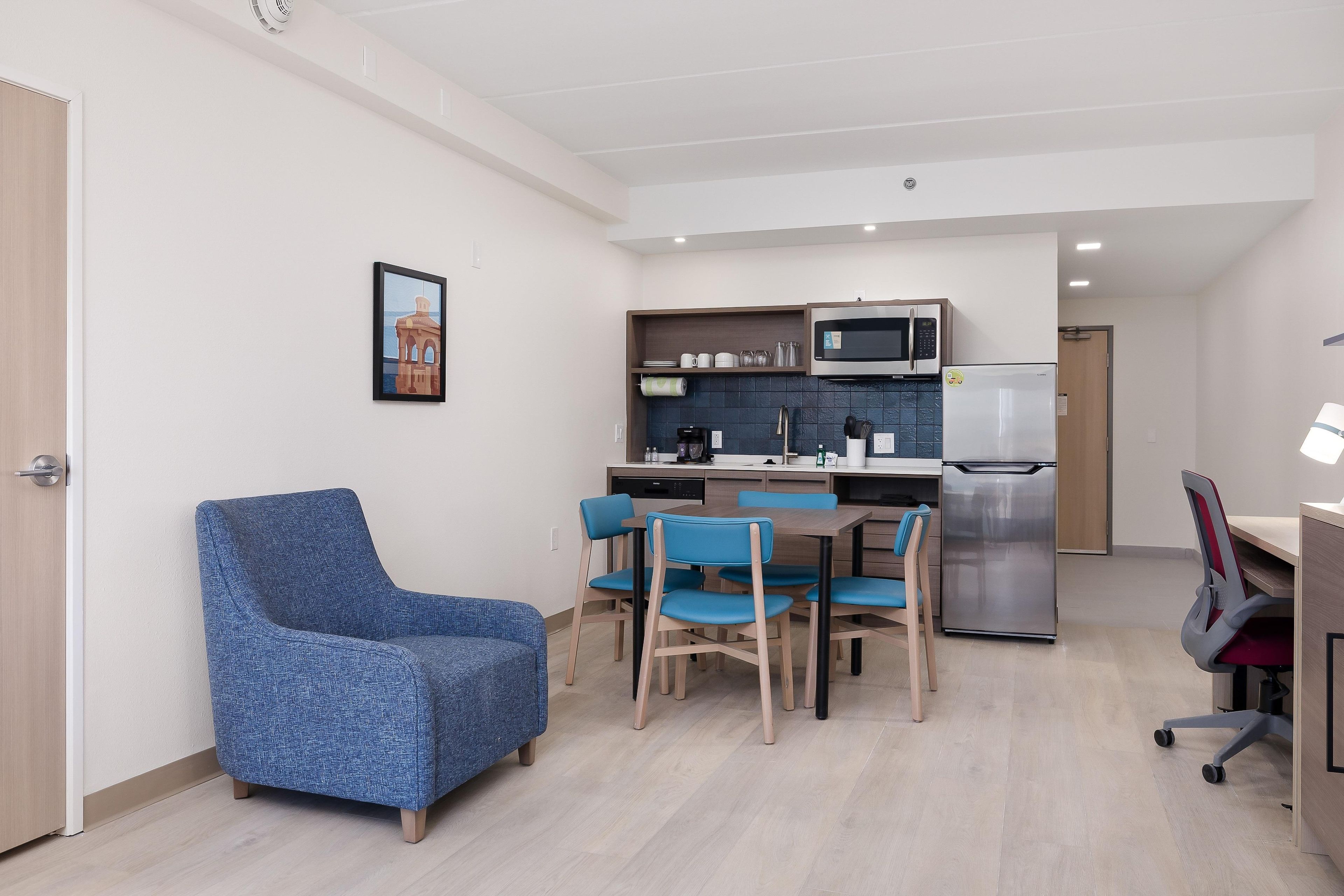 Un espace de vie compact comprenant un coin cuisine, un coin repas avec des chaises bleues et un fauteuil bleu.