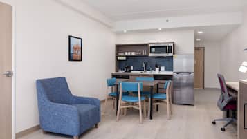 Un espace de vie compact comprenant un coin cuisine, un coin repas avec des chaises bleues et un fauteuil bleu.