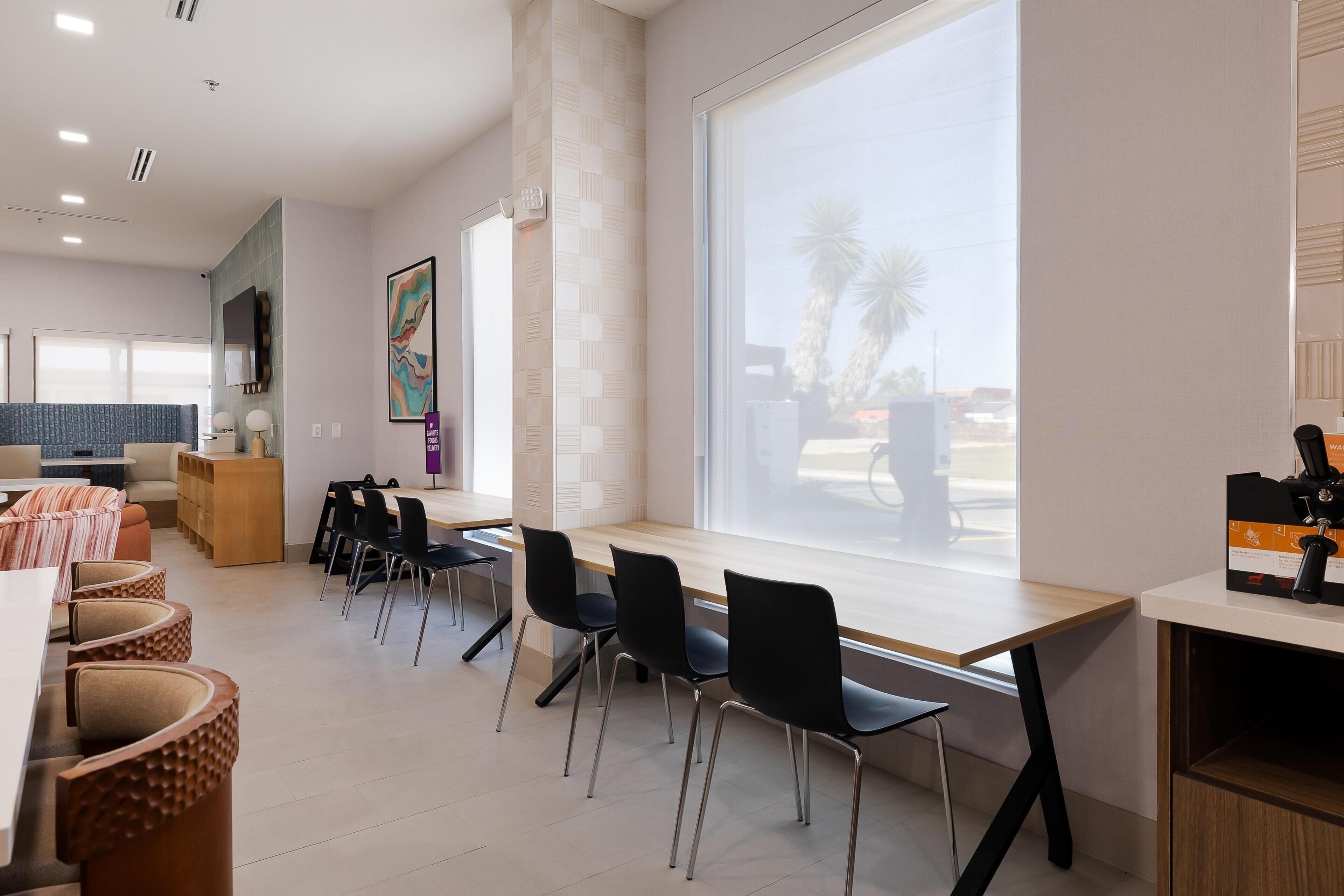A modern hotel room with a dining area, a large window with a view, and a reception desk.