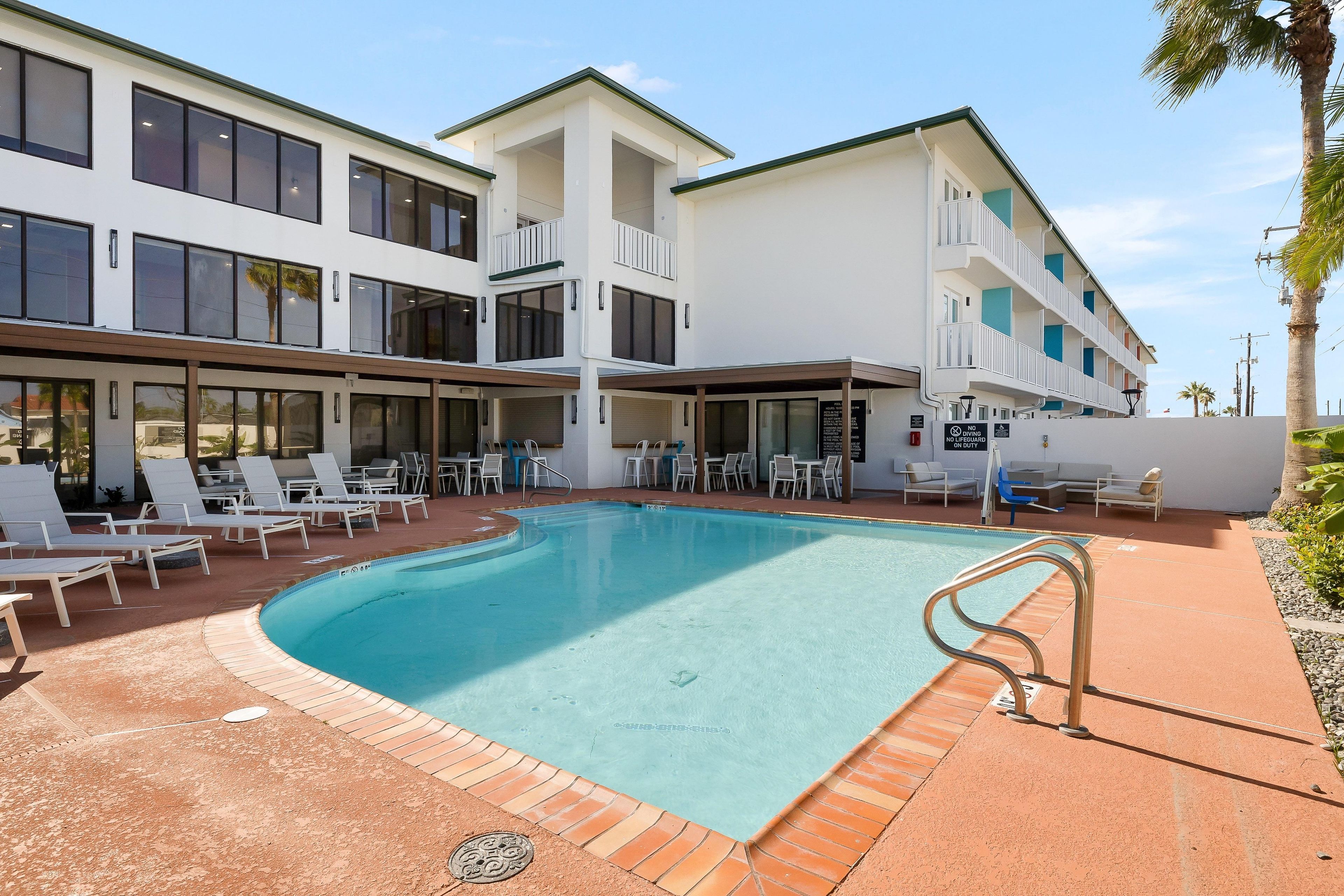 A hotel with a swimming pool, outdoor seating, and a multi-story building.