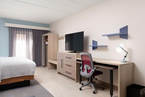 A hotel room with a bed, a desk with a computer, a chair, a TV, and a desk lamp.