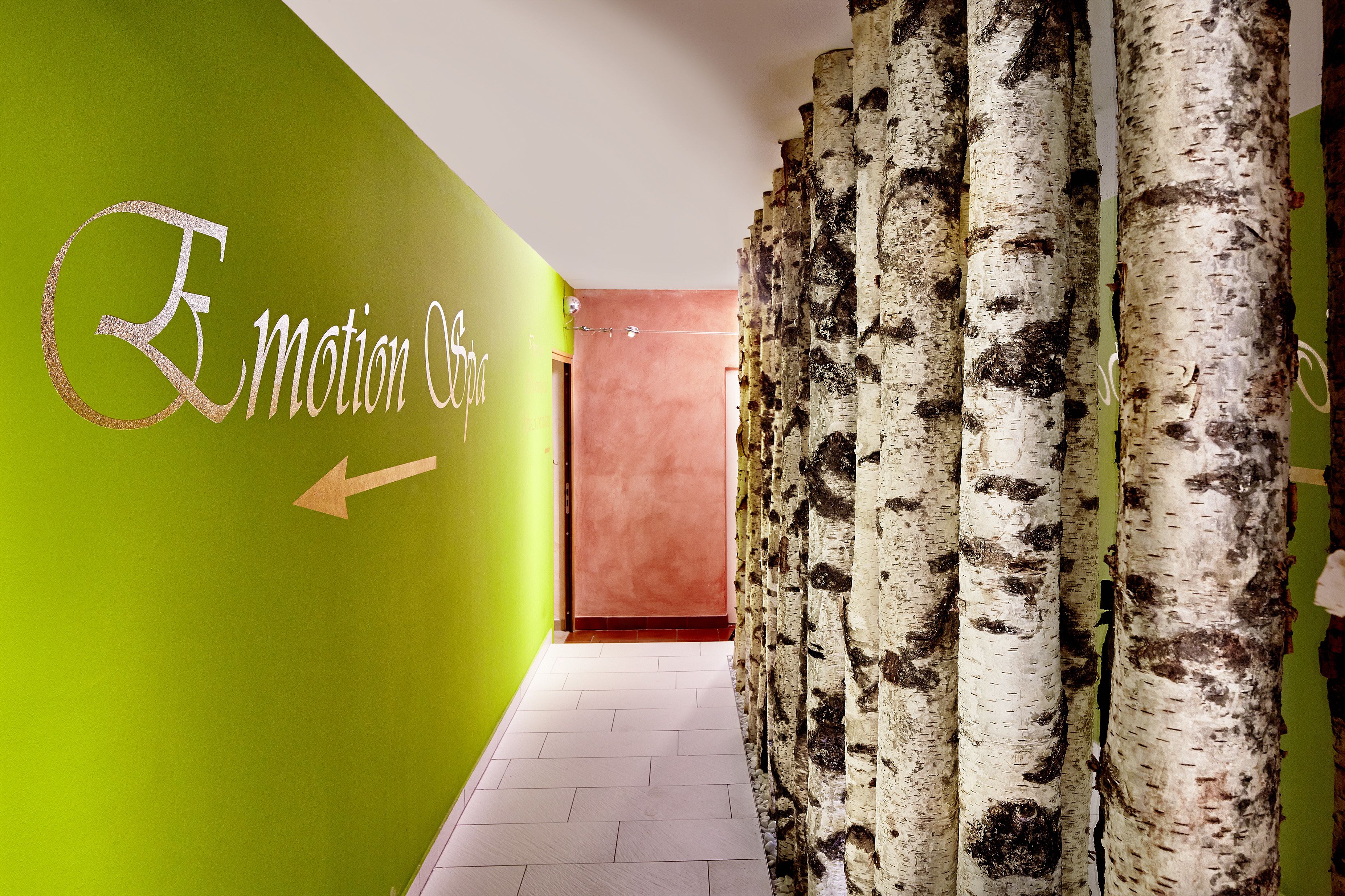 A hallway with a green wall, a sign reading "Emotion Spa", and birch tree trunks.