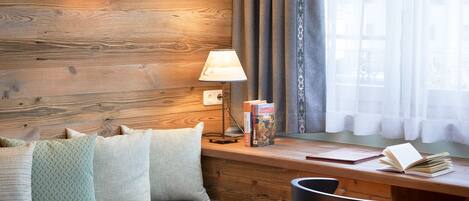 Ein gemütliches Zimmer mit Holzwand, einem Schreibtisch mit Büchern, einer Lampe und einem Fenster mit Vorhängen.