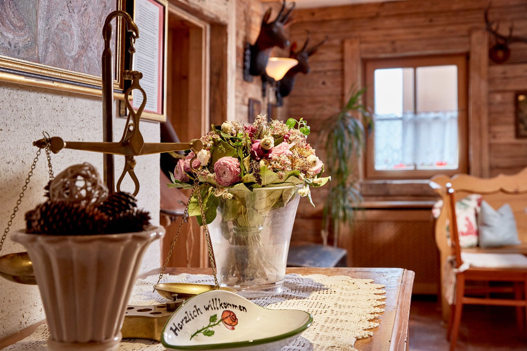 Ein rustikales Interieur mit einem Holztisch, einem Blumenstrauß, einer Waage und einem Willkommensschild.