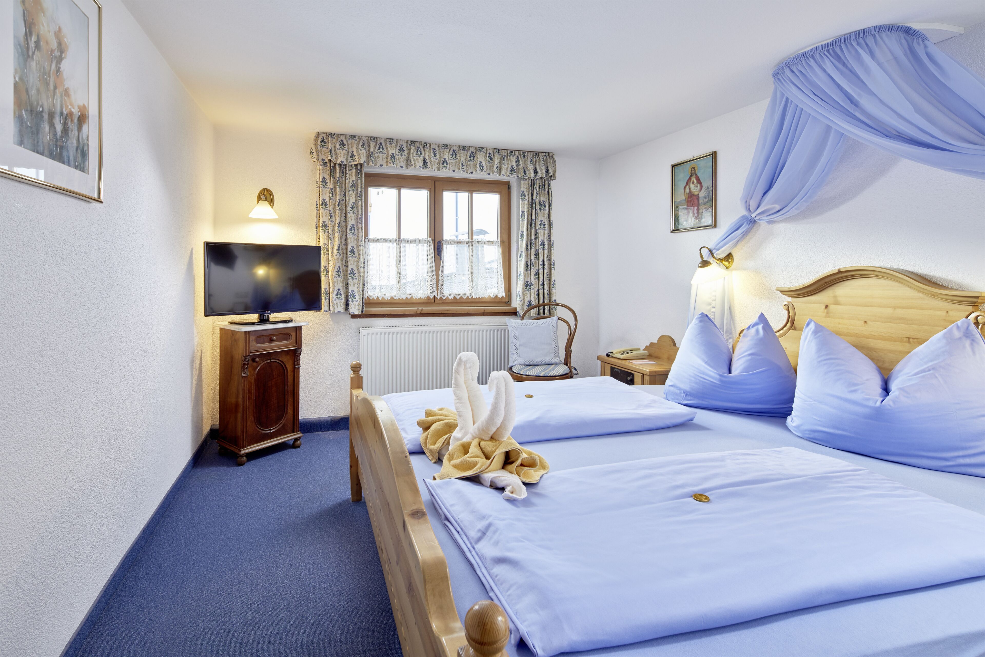 A hotel room with two beds, a wooden headboard, a window with floral curtains, a television, a wooden cabinet, and a chair.
