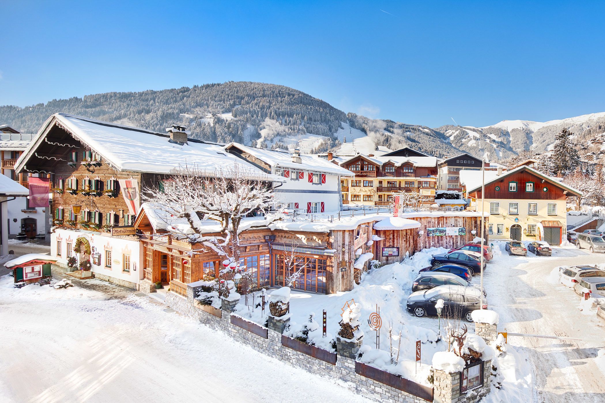 Un village enneigé, avec ses bâtiments traditionnels en bois, un ciel dégagé et une montagne en arrière-plan.