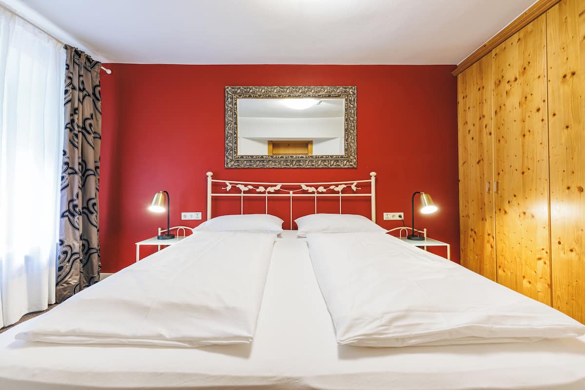 Un lit double avec une literie blanche, un mur rouge, une armoire en bois et un miroir au-dessus du lit.
