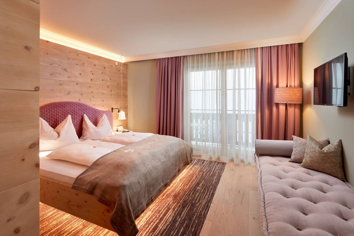 Une chambre d’hôtel avec un grand lit, un canapé, une télévision et une fenêtre avec des rideaux.