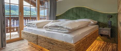 Un dormitorio con una cama grande, una mesita de noche, un cabecero verde y vistas a un balcón con barandilla de madera.