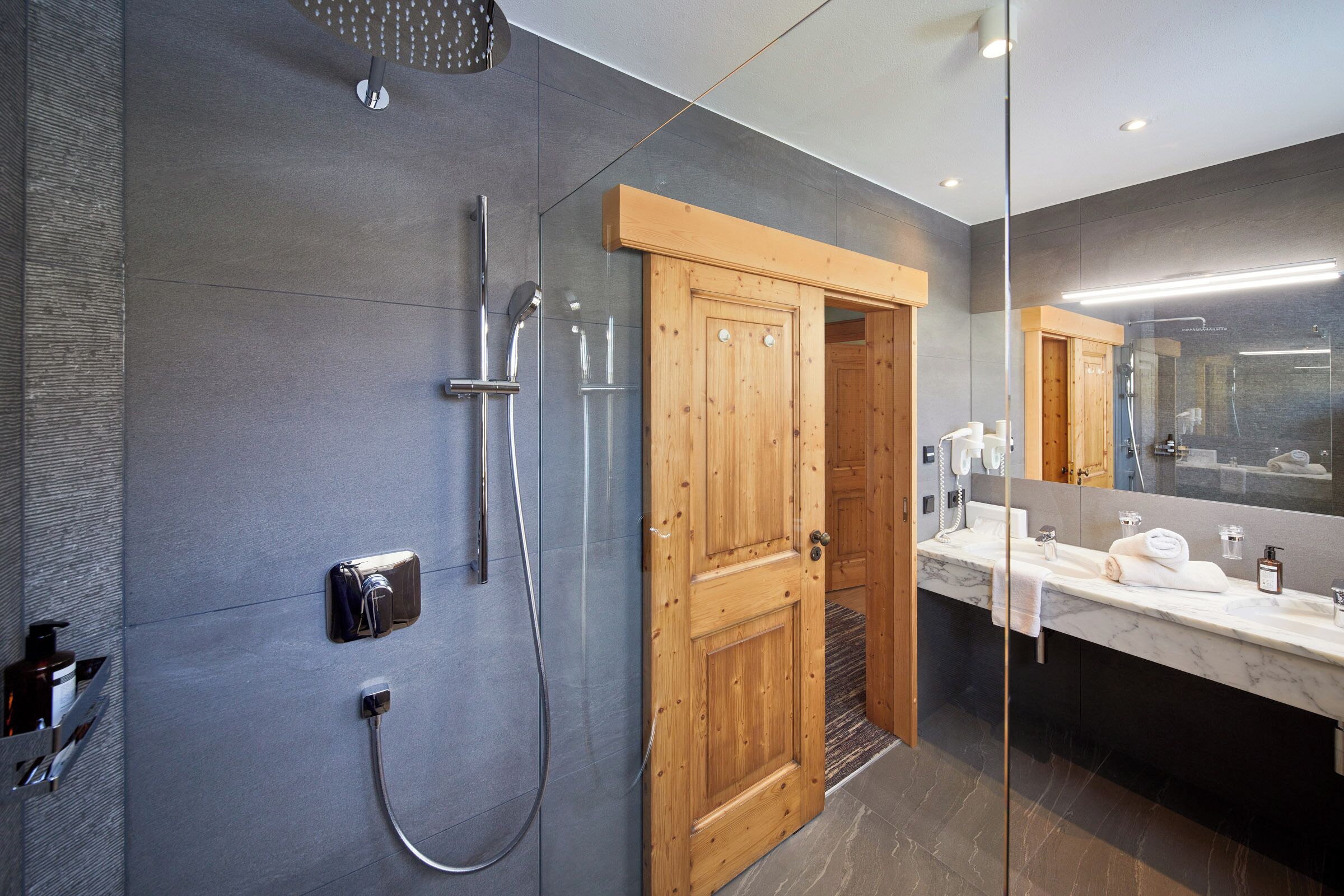 Un baño moderno con ducha, puerta de madera y tocador con espejo.