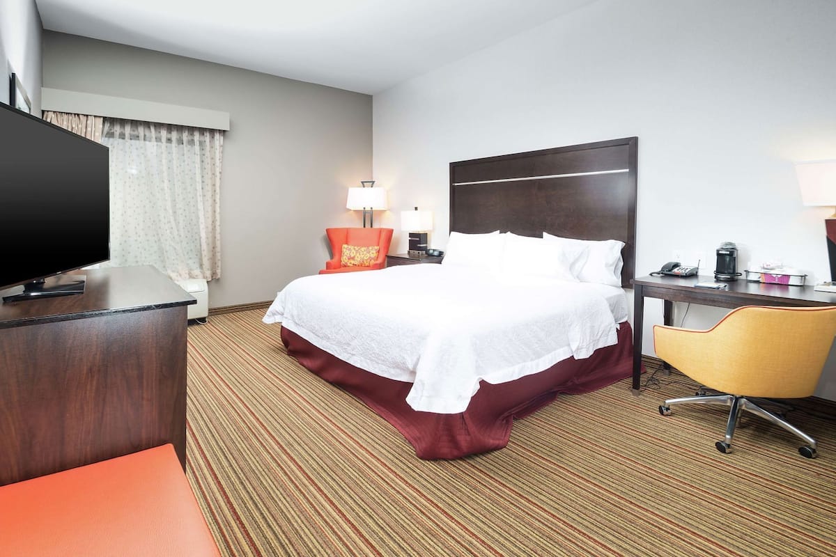 A hotel room with a bed, a desk, a chair, a television, and a lamp.