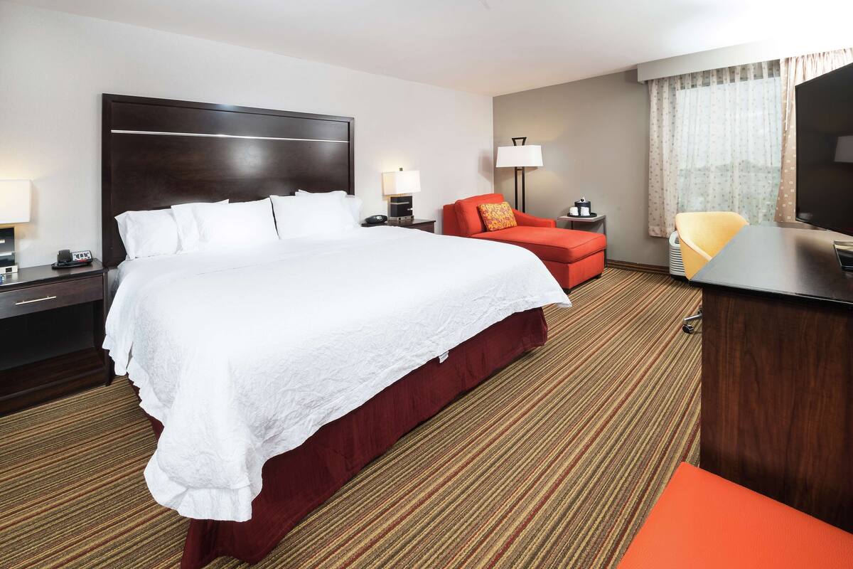 A hotel room with a large bed, a desk, a TV, and a red chair.