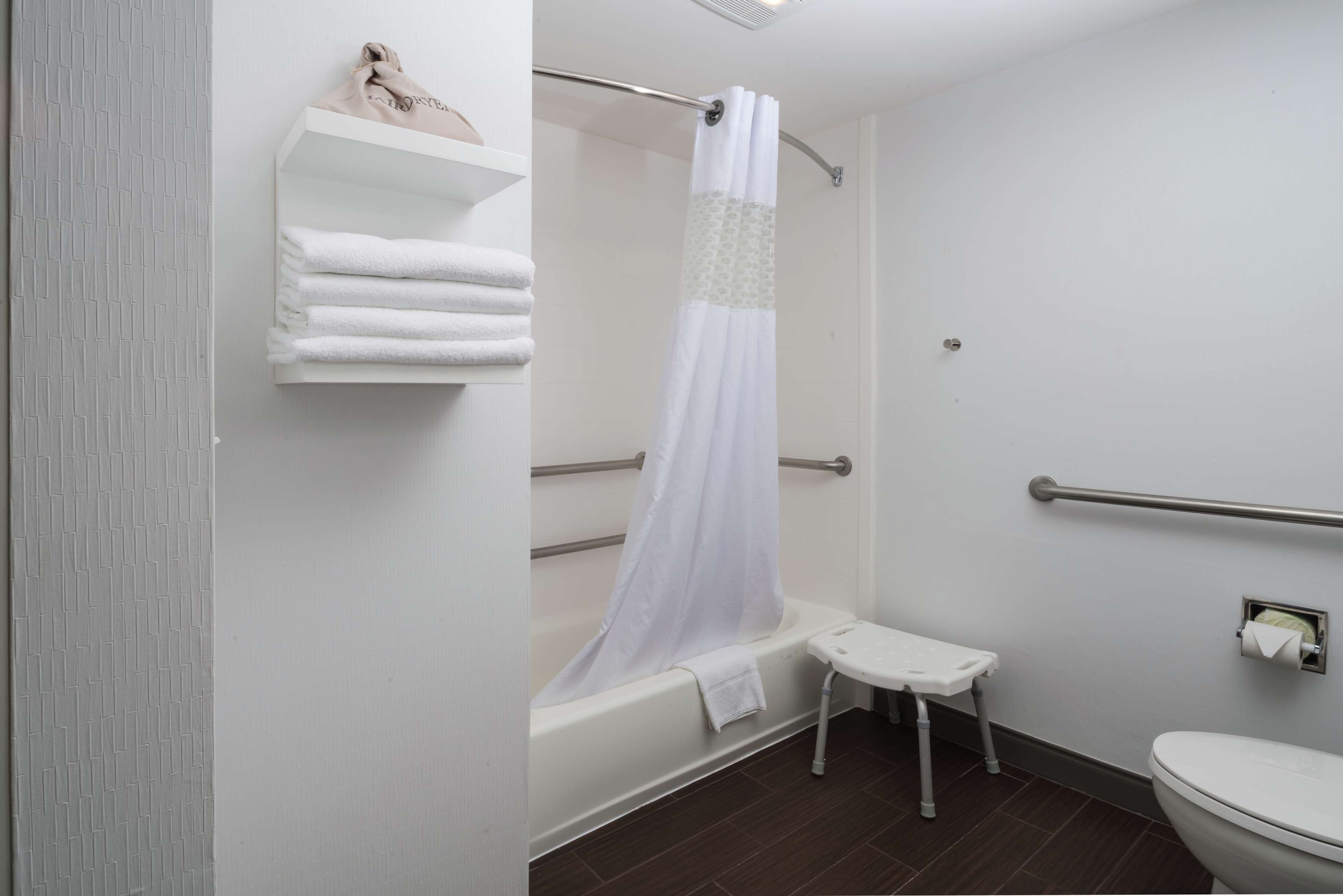 A bathroom with a bathtub, a shower curtain, a toilet, and a small step stool.