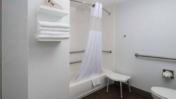 A bathroom with a bathtub, a shower curtain, a toilet, and a small step stool.
