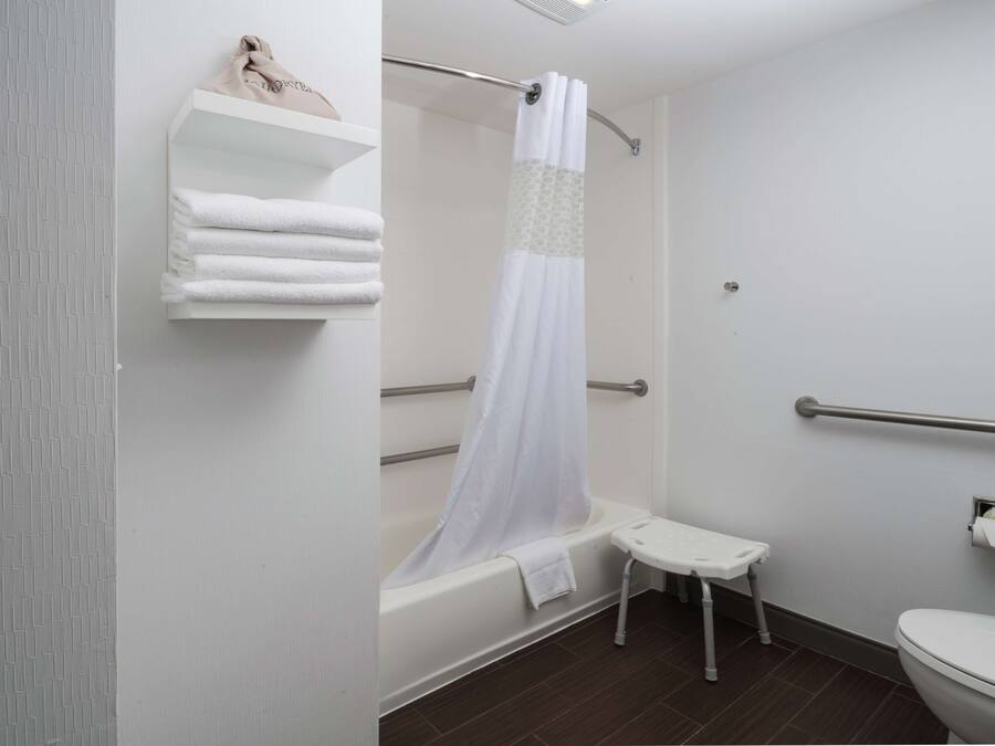 A bathroom with a bathtub, a shower curtain, a toilet, and a small step stool.