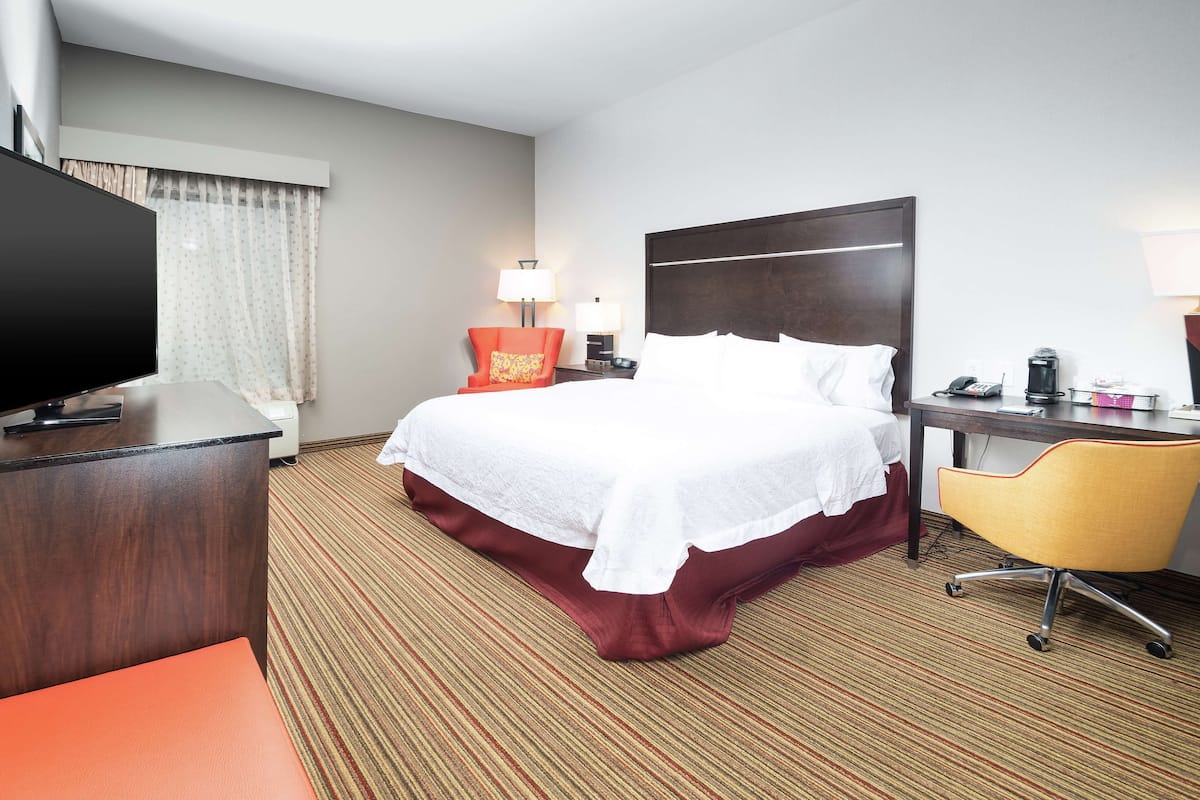 A hotel room with a large bed, a desk with a computer, a chair, and a television.