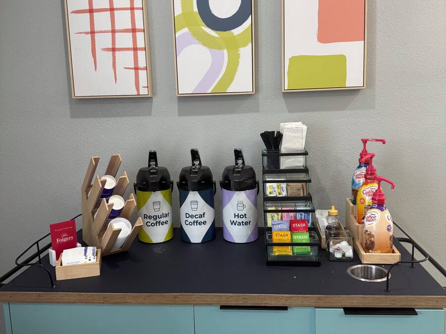 A coffee station with dispensers labeled 'Regular Coffee,' 'Decaf Coffee,' and 'Hot Water,' along with a coffee machine and a bottle of coffee-mate.