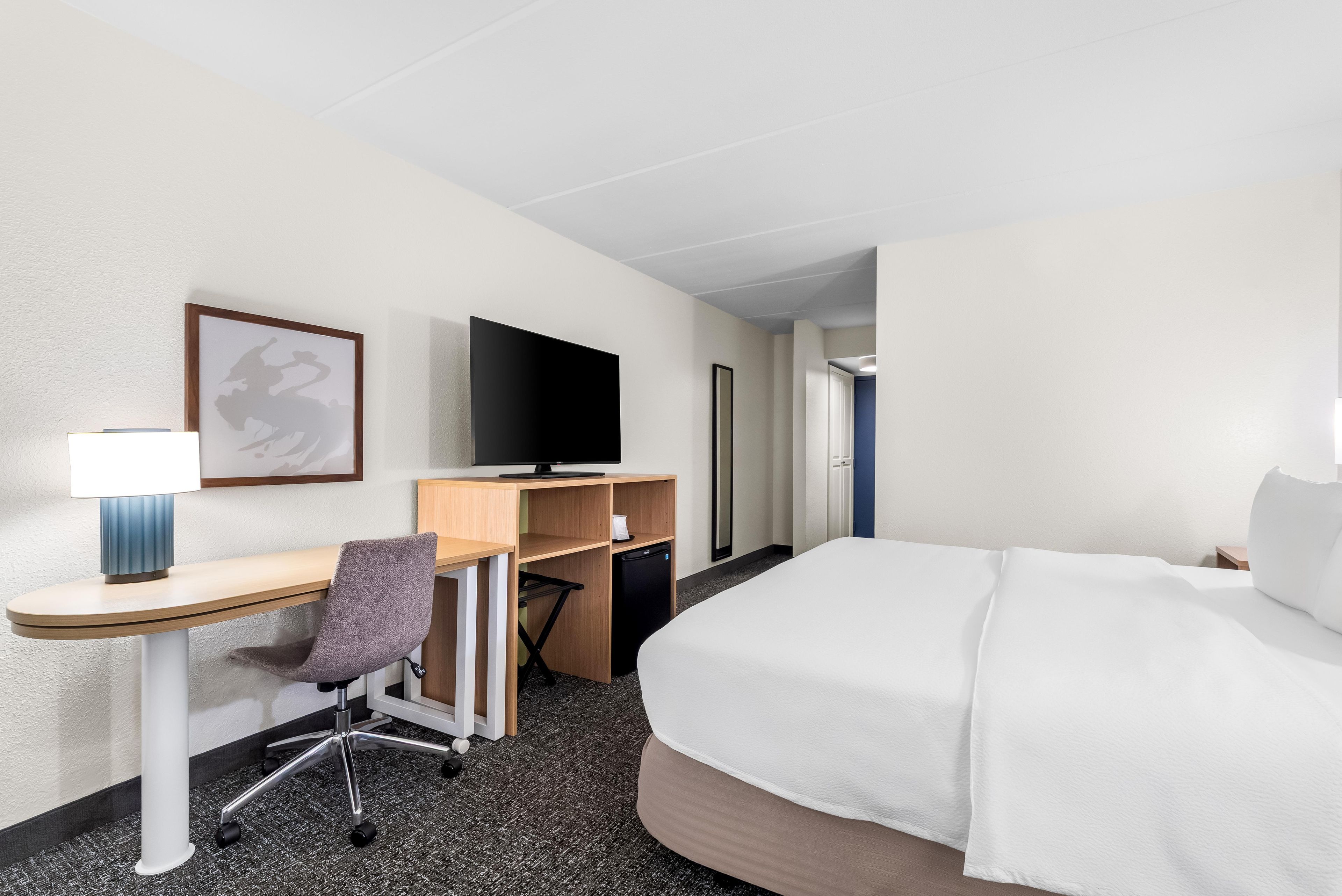 Hotellihuone, jossa on sänky, työpöytä, tuoli, televisio ja seinällä kehystetty taulu.