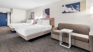 A hotel room with two beds, a sofa, a small table, and artwork on the walls.