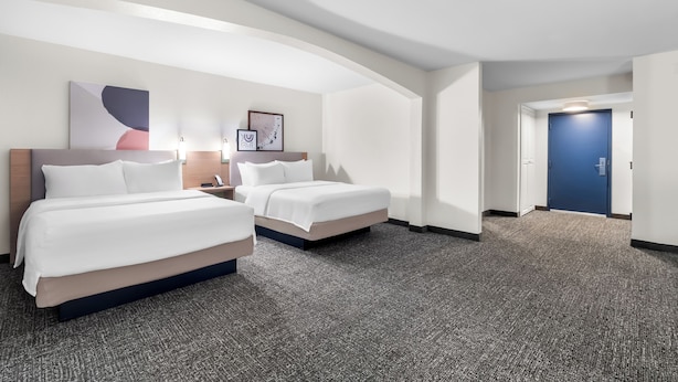 A hotel room with two beds, a large abstract painting, and a blue door.