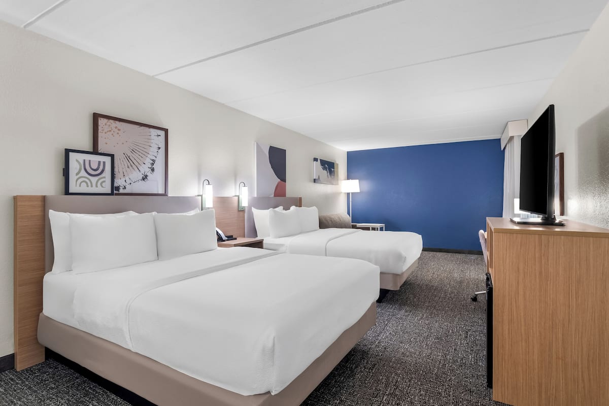 A hotel room with two beds, a desk, a TV, and artwork on the walls.