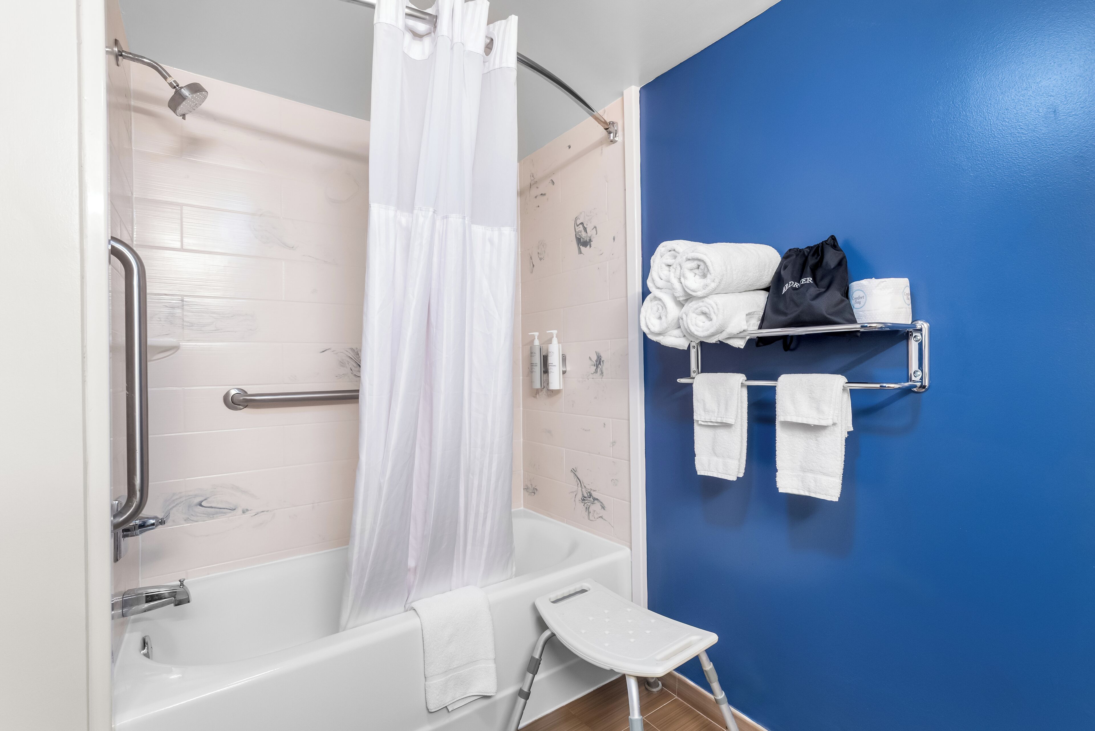 Een badkamer met een bad, een douchegordijn, een handdoekrek met handdoeken en een klein opstapkrukje.