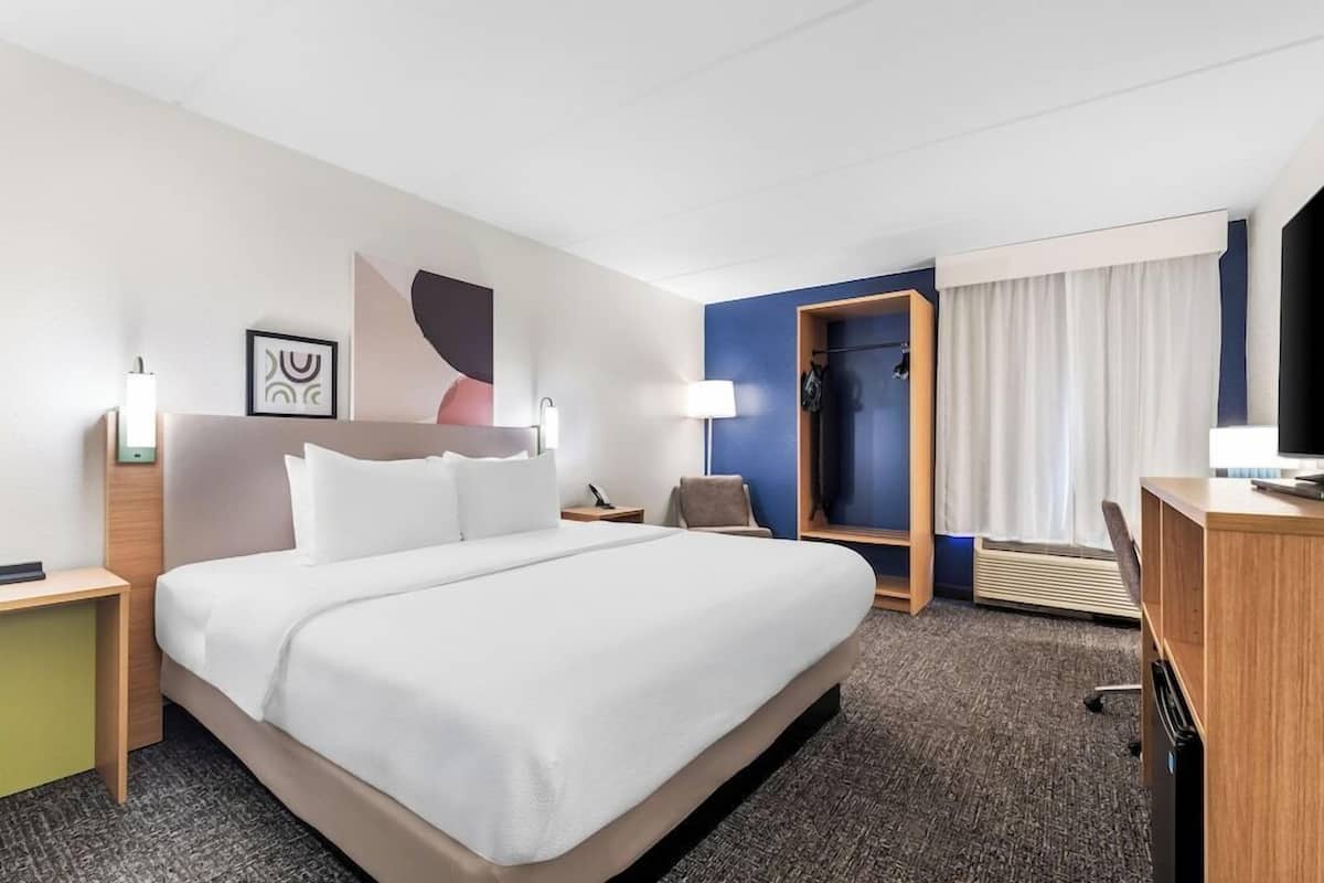 A hotel room with a large bed, bedside tables, a desk, a chair, a TV, and a wardrobe.