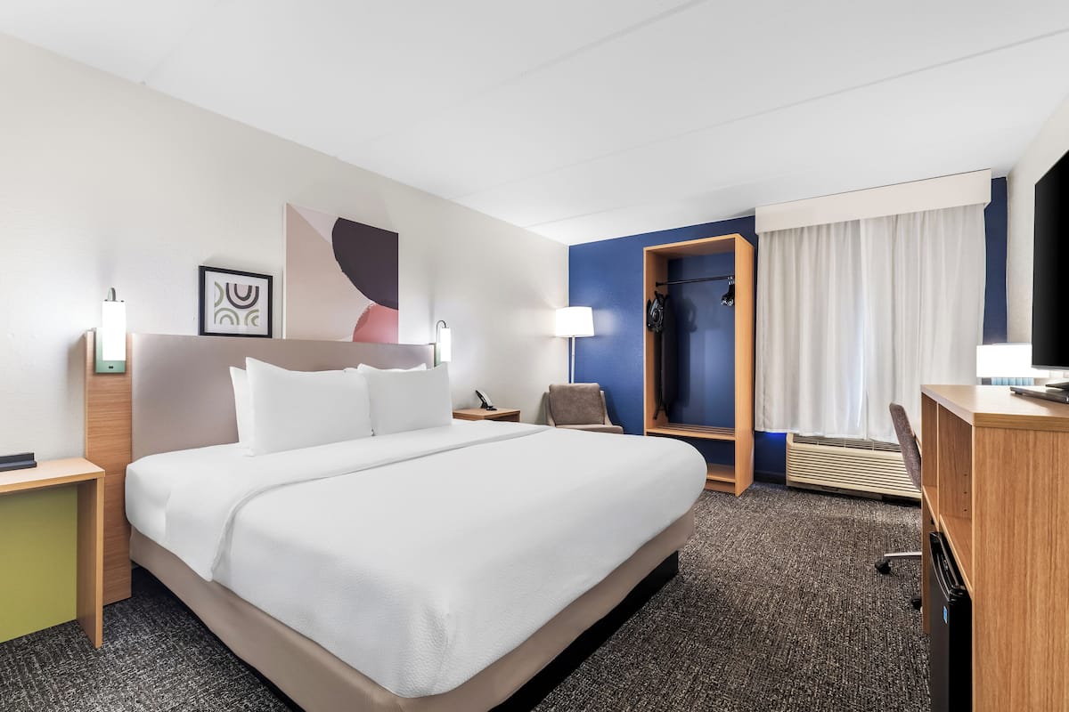 A hotel room with a large bed, a desk, a chair, a TV, and a bathroom door.