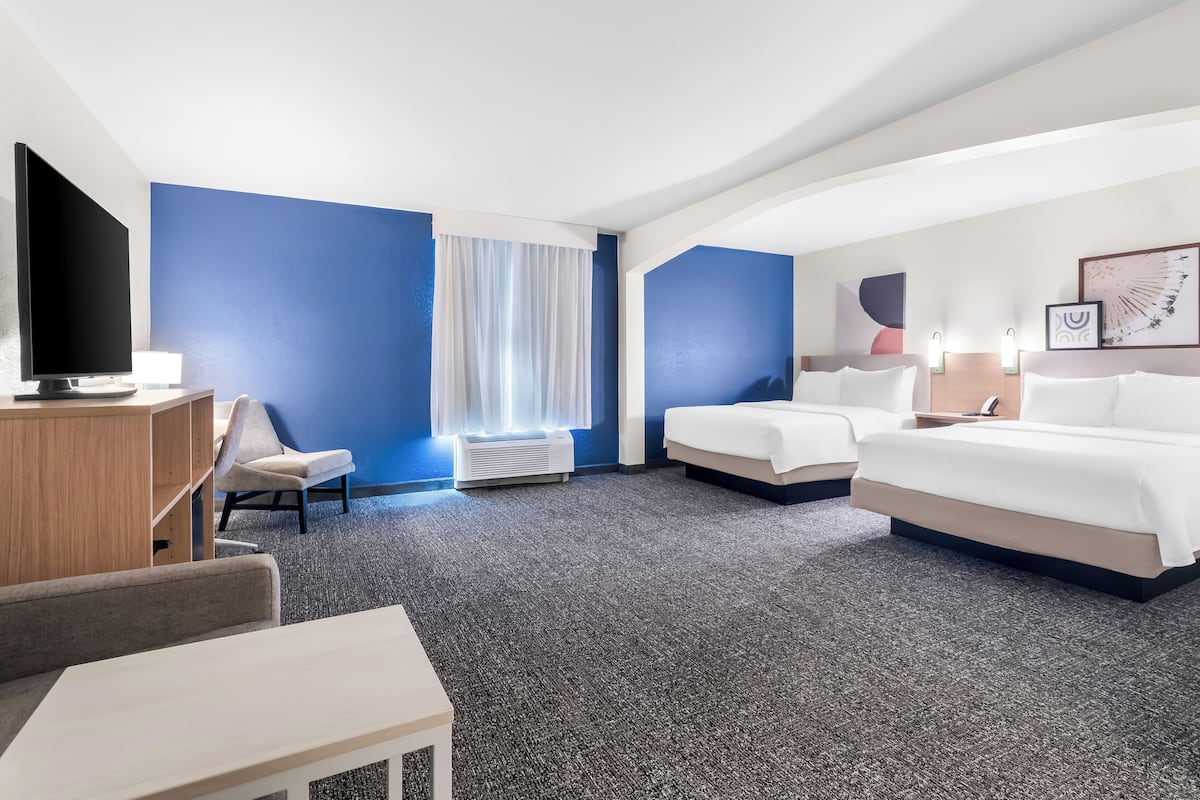 A hotel room with a large bed, a smaller bed, a desk with a TV, a chair, and a window with curtains.