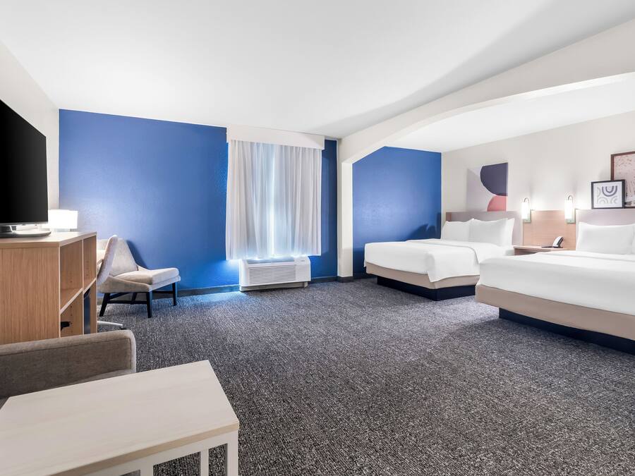 A hotel room with a large bed, a smaller bed, a desk with a TV, a chair, and a window with curtains.