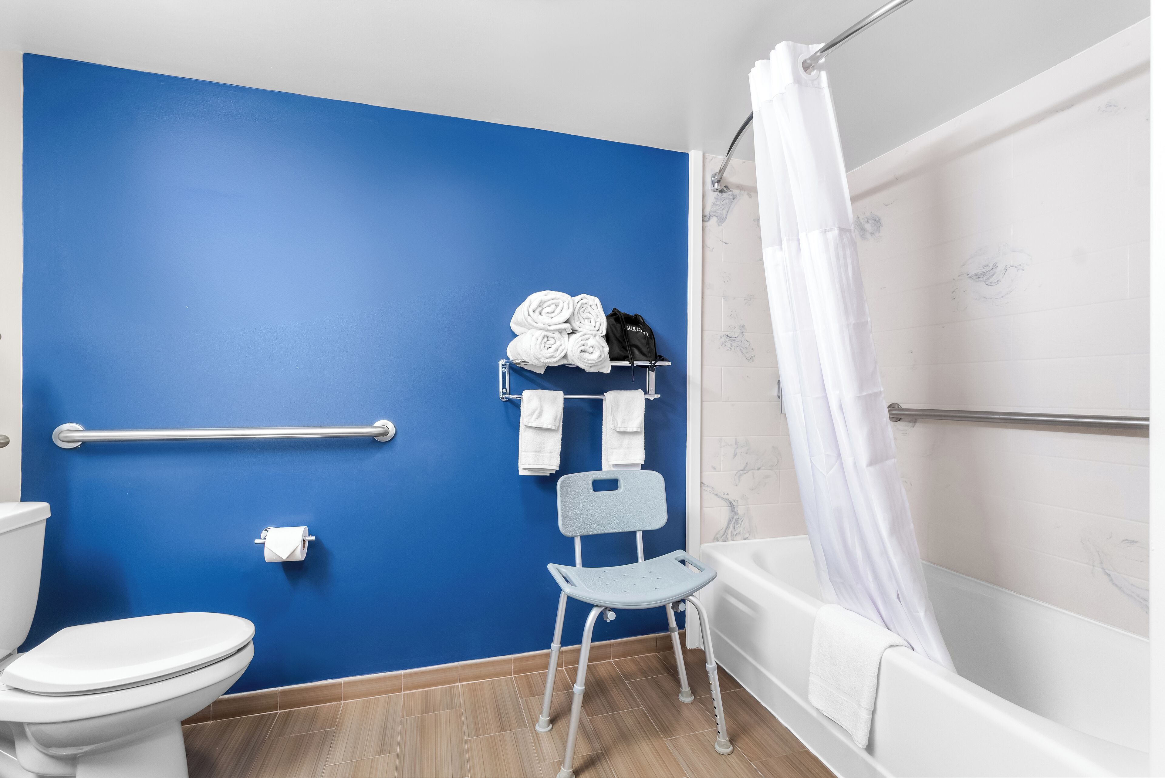 A bathroom with a blue wall, white toilet, and bathtub.