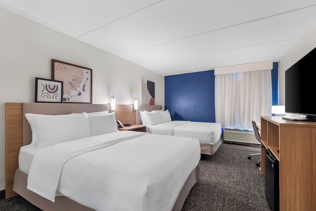 A hotel room with two beds, a desk, a TV, and artwork on the wall.