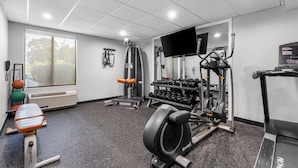 A gym with cardio machines, weightlifting equipment, and a TV screen.