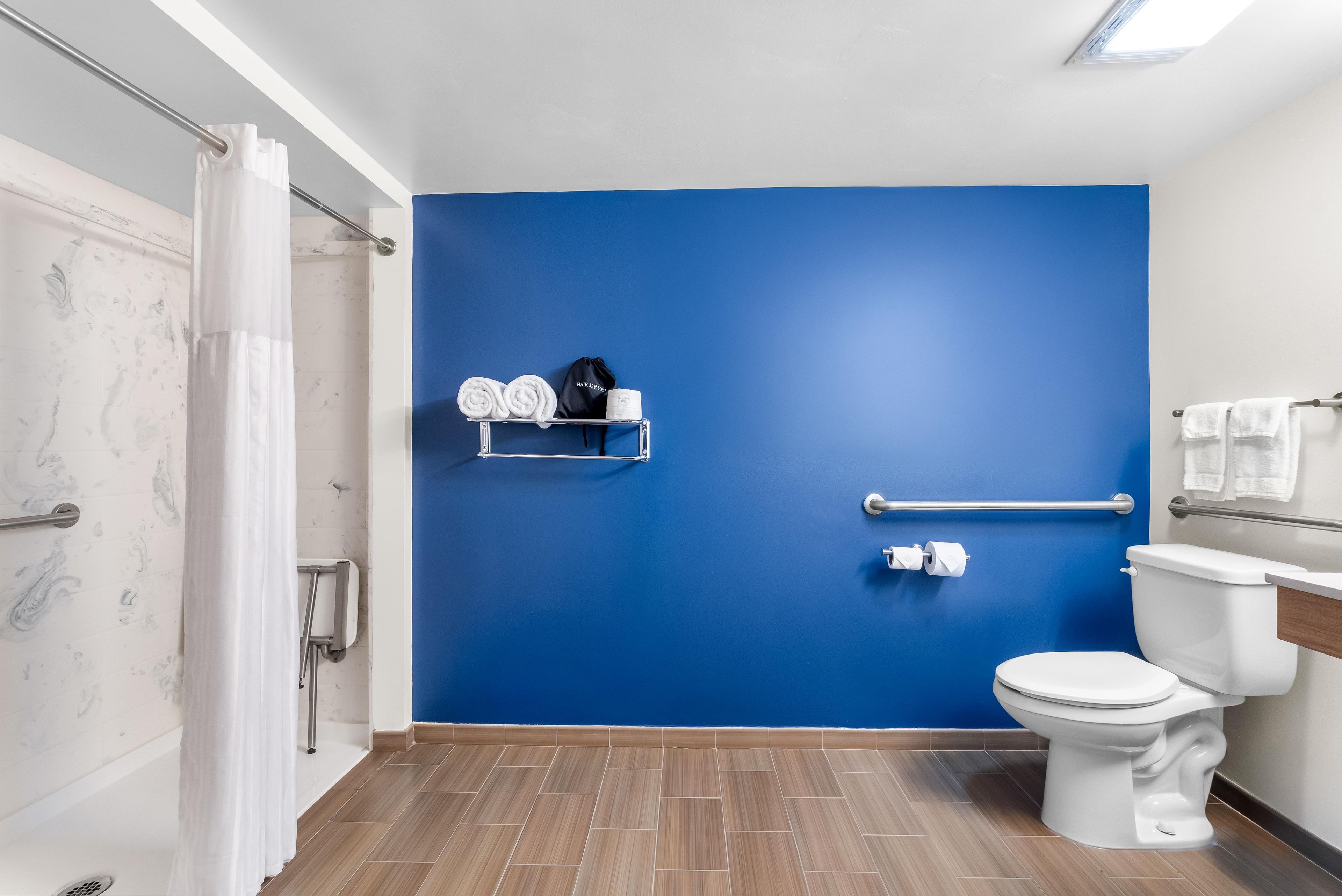 A bathroom with a blue wall, a white toilet, a shower area, and a towel rack with towels and a hair dryer.