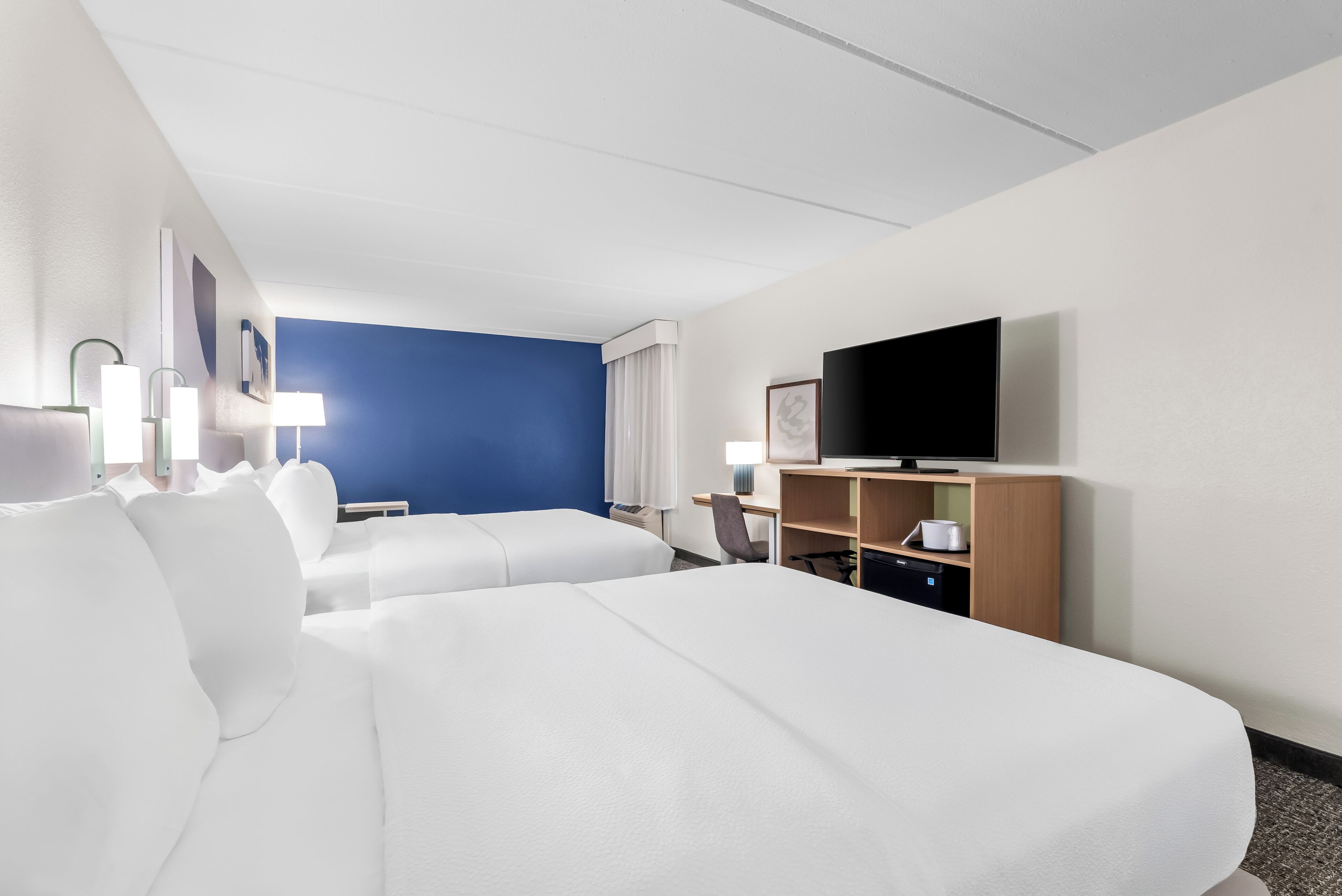 Une chambre d’hôtel avec deux lits, un bureau, une télévision et une fenêtre avec des rideaux.