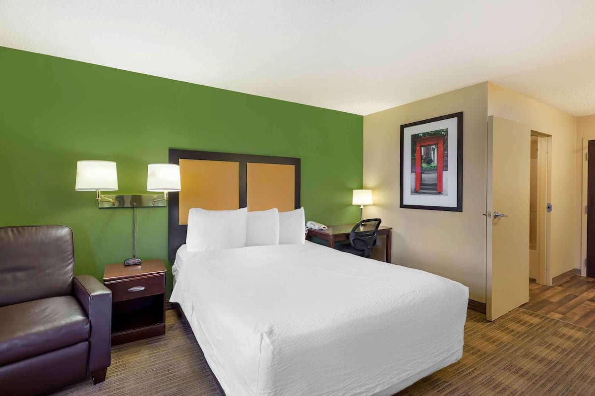 A hotel room with a large bed, a desk, a chair, a nightstand, and a green accent wall.