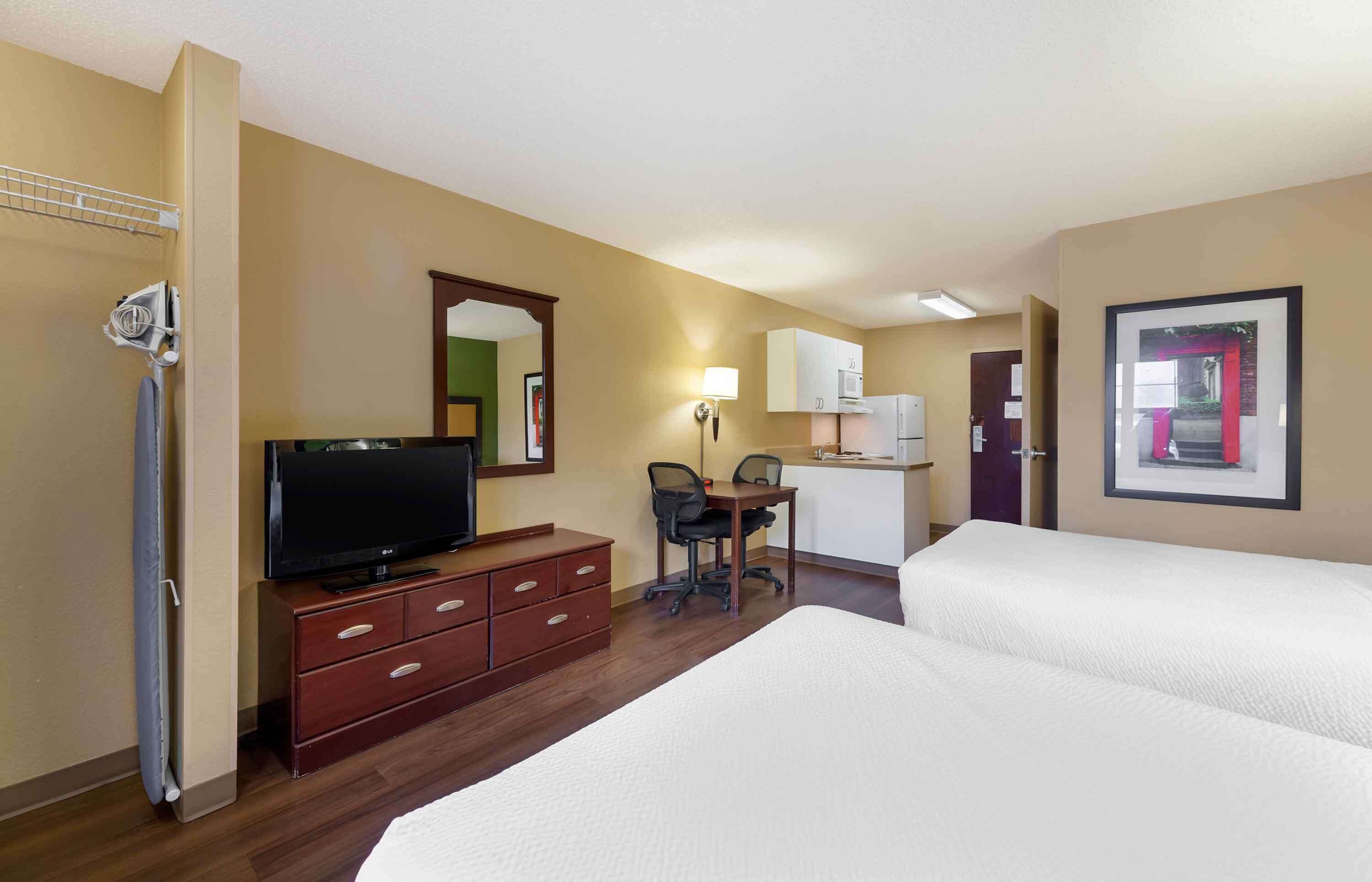 Une chambre d’hôtel avec deux lits, un bureau avec une chaise, une télévision, un four à micro-ondes et une petite kitchenette.