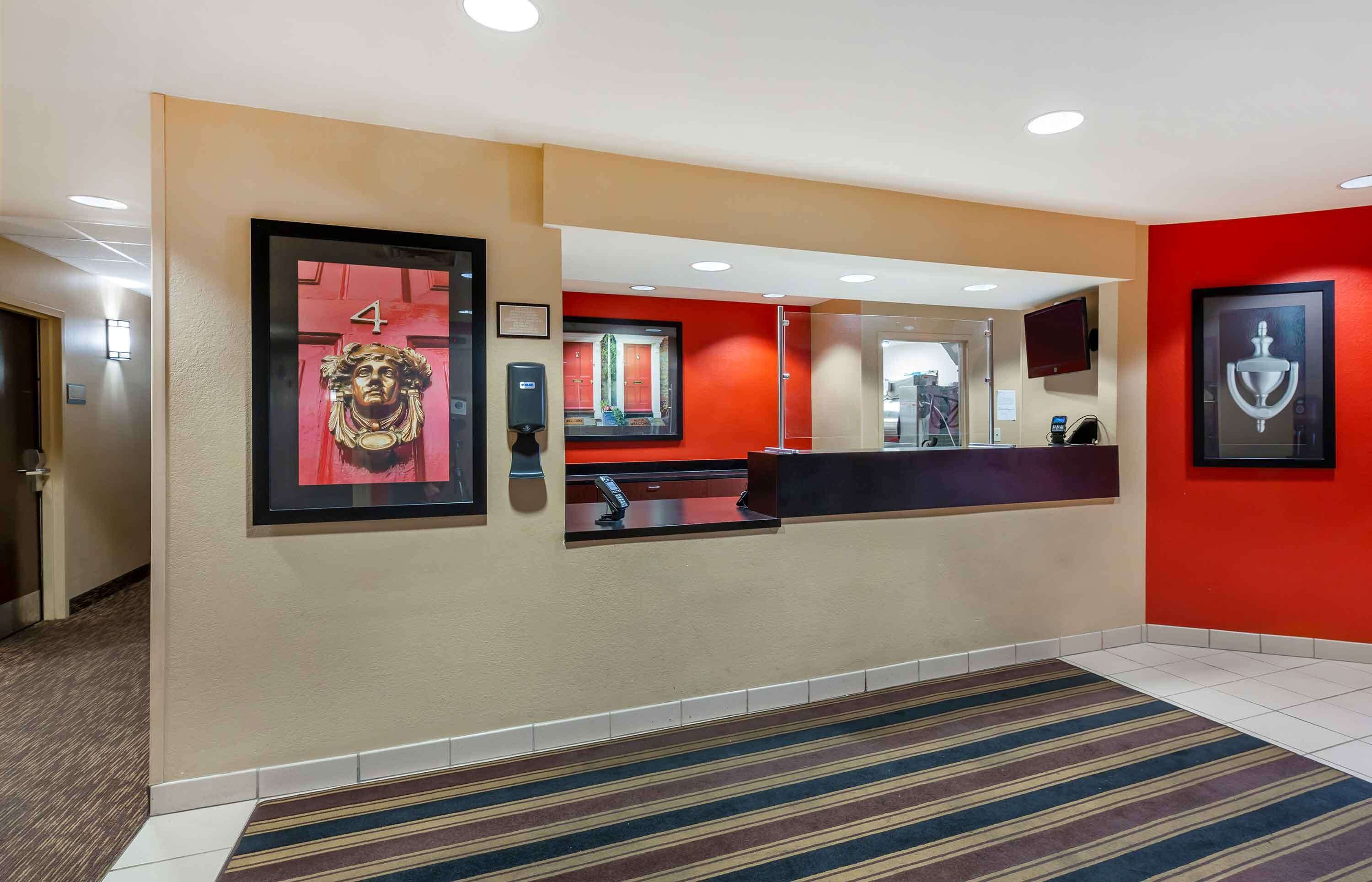 Un espace d’accueil d’hôtel comprenant un comptoir de réception, une enseigne portant le chiffre « 4 », un miroir et une œuvre d’art encadrée accrochée au mur.