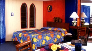 Une chambre d’hôtel avec un lit, un bureau et une chaise. Il y a une fenêtre avec des rideaux, une lampe et une horloge au mur.
