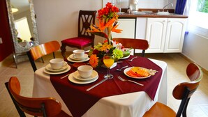 Une table à manger dressée avec des assiettes, des bols, des couverts et une salade de fruits.