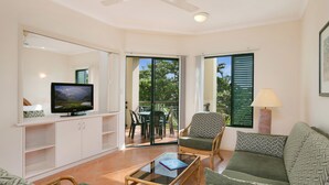 A living room with a television, sofa, armchair, and coffee table. - Tropic Towers Apartments (Cairns North)