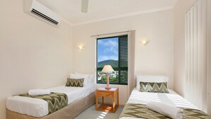 A hotel room with two single beds, a small wooden nightstand with a lamp, and a window with a view of a mountain and a cityscape. - Tropic Towers Apartments (Cairns North)